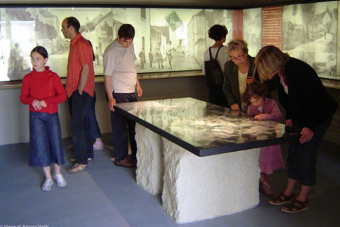dans une salle de la Maison du Souvenir à Maillé, un groupe de visiteurs se penche sur une carte en relief