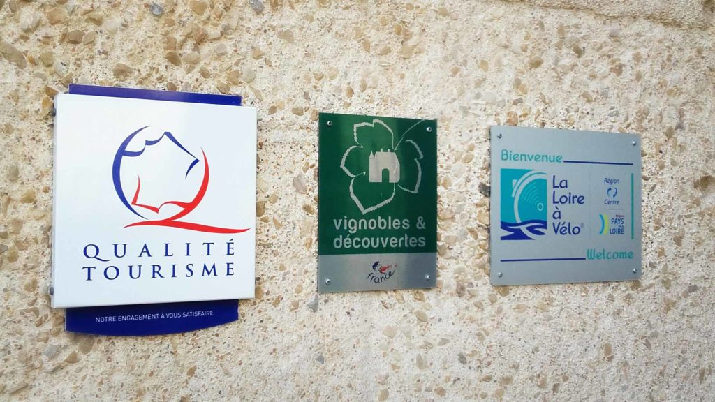 Trois pannonceaux de labels touristiques (Qualité tourisme, vignobles et découvertes et Loire à Vélo) sont accrochés sur un mur