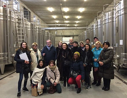 Un groupe de personnes prend la pose entre les cuves de vin dans un chais