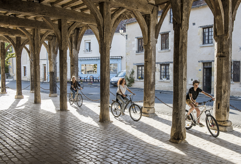 Un groupe de trois cyclistes circulent sous les halles médiévales de Montrésor